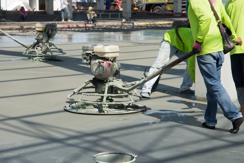 Workers smoothing out the surface of new concrete slab using power tools - Quillen Construction Group