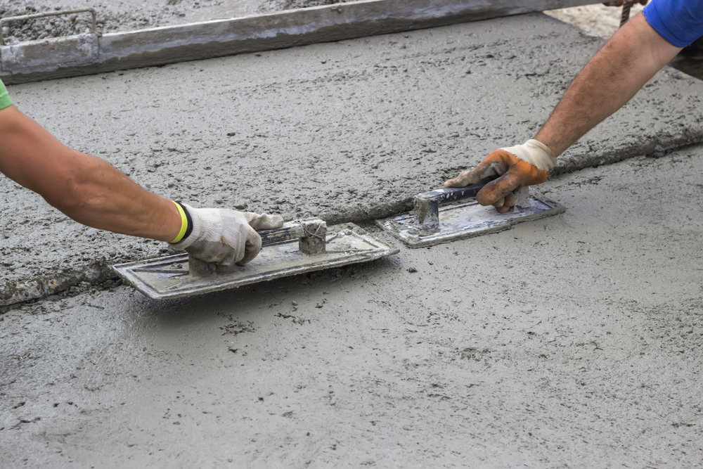 Workers using hand tools to float the edges and perimeters of a new slab being poured - Quillen Construction Group