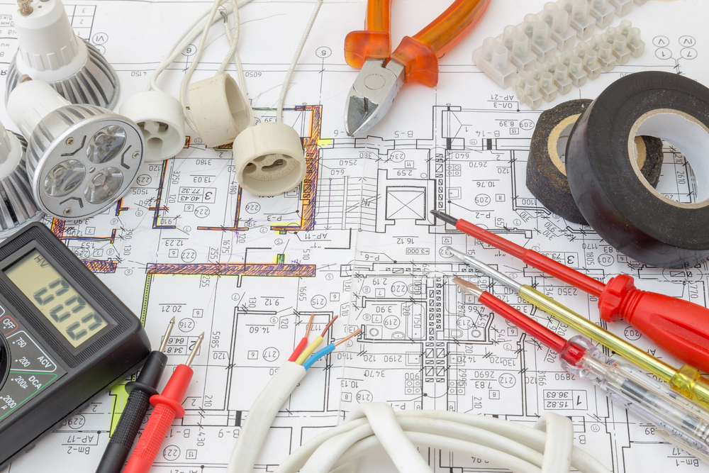 Electrical parts and tools sitting on top of building blueprints during construction of a home - Quillen Construction Group