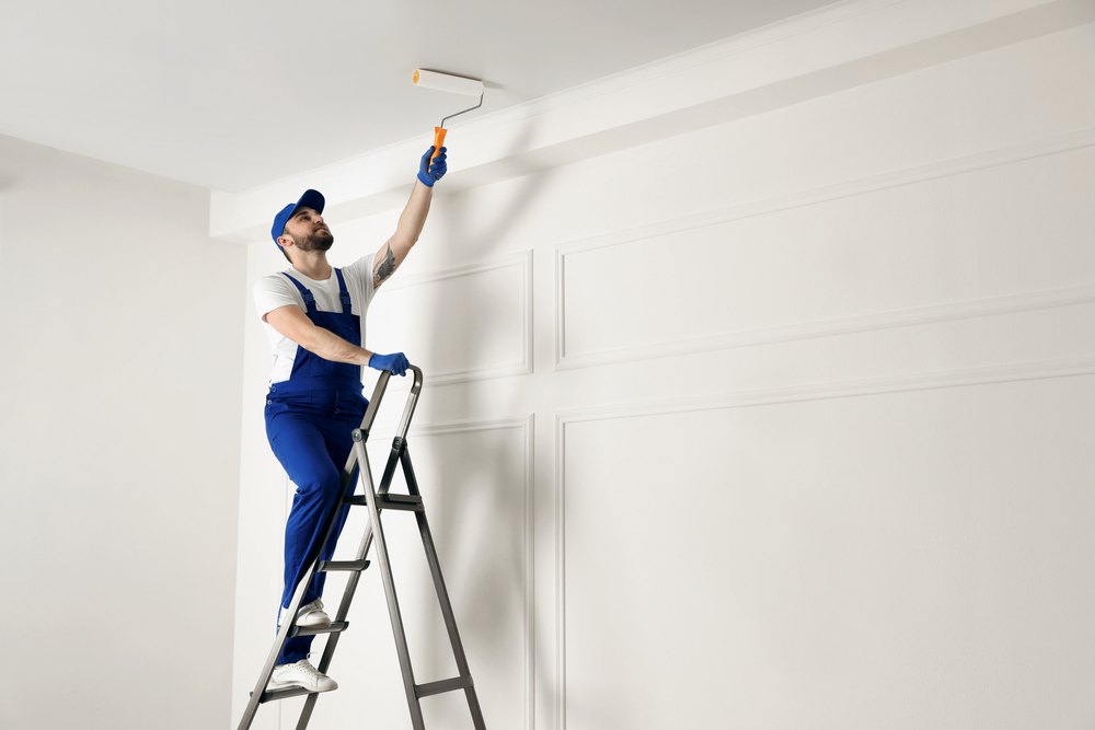 Painter on medium ladder with roller painting ceiling - Quillen Construction Group