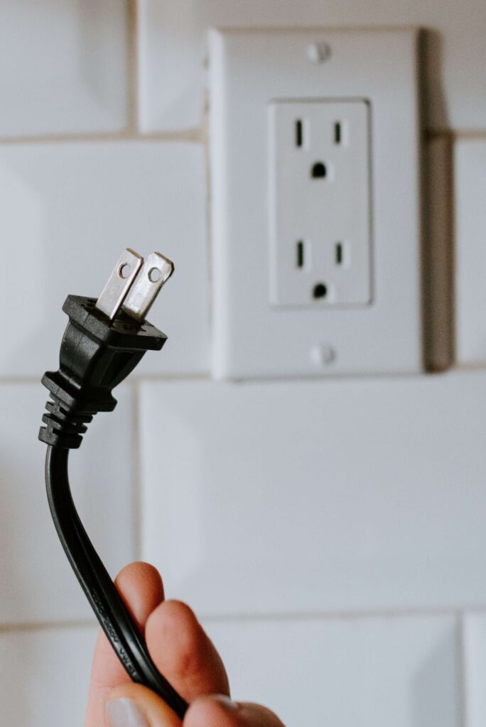 Image of person holding electrical cord next to a power outlet.