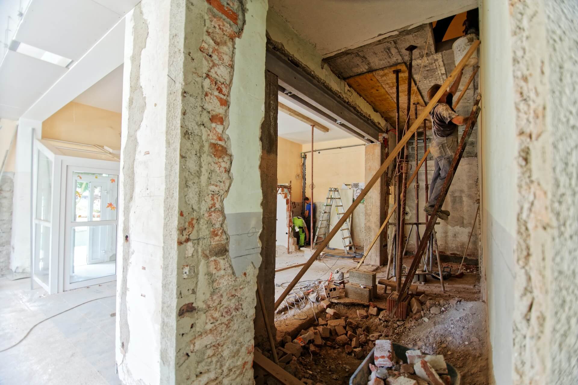 worker standing on a ladder, handing a bucket up to another worker