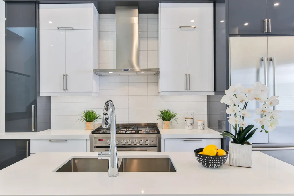 Kitchen Remodel New Orleans - An image of a modern kitchen with white & off-navy cabinets, quartz countertops, stainless steel hood & range, farmhouse style sink.