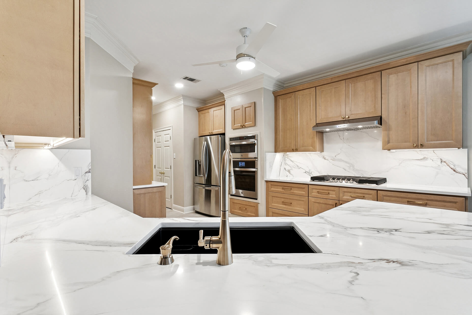 Modern kitchen with wood cabinets, stainless steel appliances, marble countertops and backsplash, an undermount sink with gooseneck faucet, and ceiling fan. This Slidell, LA Kitchen Remodeling project is well-lit and impeccably organized.