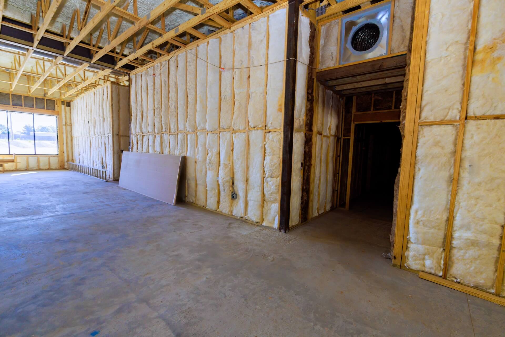 Interior of a commercial construction project in Waggaman, Louisiana, featuring exposed wooden framing, insulated walls, a concrete floor, and drywall leaning against the wall. Natural light streams through large windows.